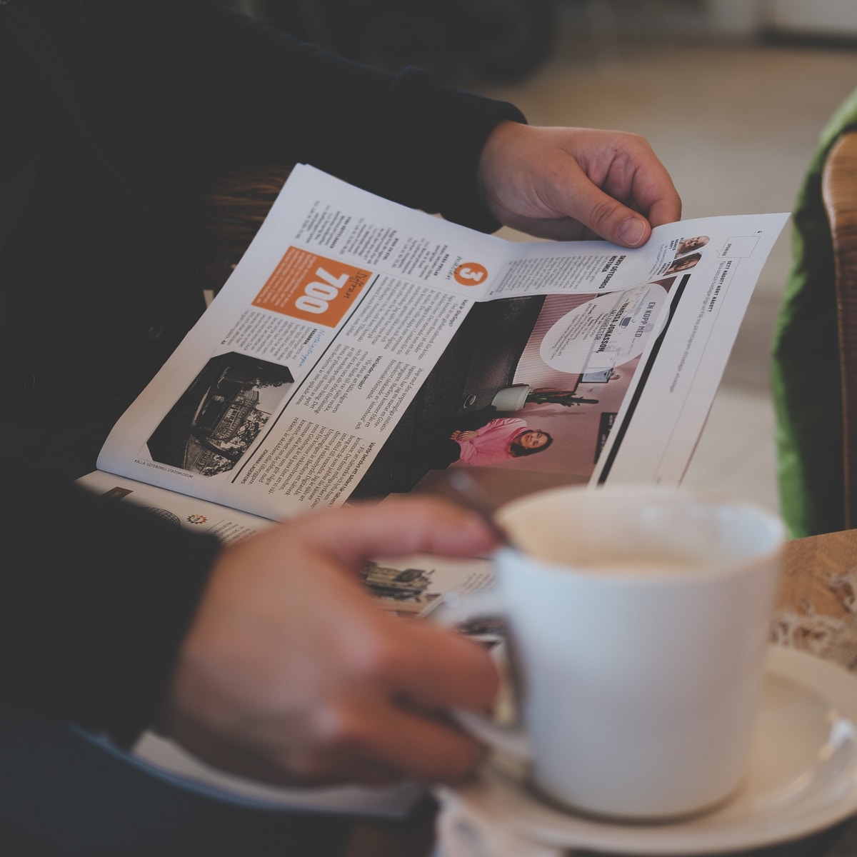 person reading while holding white ceramic mug