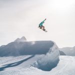 man in black jacket and blue denim jeans jumping on snow covered mountain during daytime